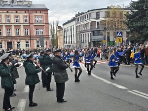 osoby maszerują, dużo flag Polski, pochmurno, widać poczet sztandarowy