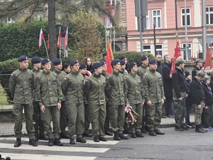 osoby maszerują, dużo flag Polski, pochmurno, widać poczet sztandarowy