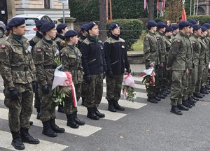 osoby maszerują, dużo flag Polski, pochmurno, widać poczet sztandarowy