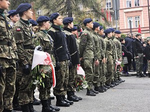 osoby maszerują, dużo flag Polski, pochmurno, widać poczet sztandarowy