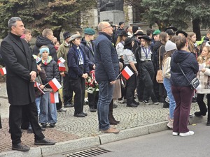 osoby maszerują, dużo flag Polski, pochmurno, widać poczet sztandarowy