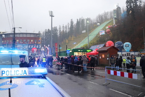 zmierzch, pochmurno, pojazd policji z sygnałami, w tle skocznia narciarska i tłumy ludzi