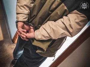 mężczyzna z kajdankami na rekach z tyłu, wchodzi do pomieszczenia