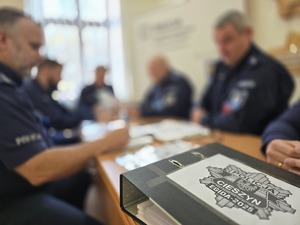 teczka z napisem Egida, w tle policjanci