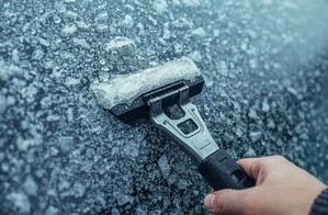 dłoń prowadzi skrobaczkę do szyb po zalodzonej szybie samochodowej