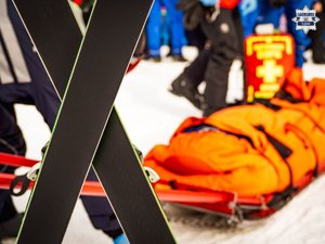 zdjęcie -skrzyzowane narty, śnieg, zima, w tle nosze ratownicze