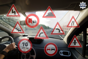 grafika przedstawiająca widok z wnętrza samochodu, widoczne liczne znaki drogowe