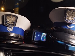 policyjne czapki, między nimi fotoradar ze zdjęciem i pomiarem prędkości 105 kilometrów na godzinę