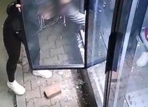 zdjecie-noc, wybita szyba, cegłówka na ziemi, kobieta sięga po kwiaty