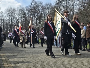 Dzień, słonecznie, plac przed pomnikiem, ludzie zebrani na uroczystości - przedstawiciele służb mundurowych, uczniowie szkół, mieszkańcy, widoczne flagi Polski oraz sztandary