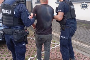 Umundurowani policjanci prowadzą osobę zatrzymaną.