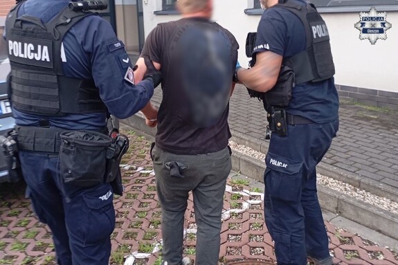 Umundurowani policjanci prowadzą osobę zatrzymaną.