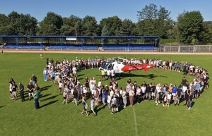 stadion. ludzie na murawie zebrani wokół helikoptera, słonecznie