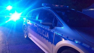 radiowóz policji w nocy, ma włączone niebieskie światła uprzywilejowania